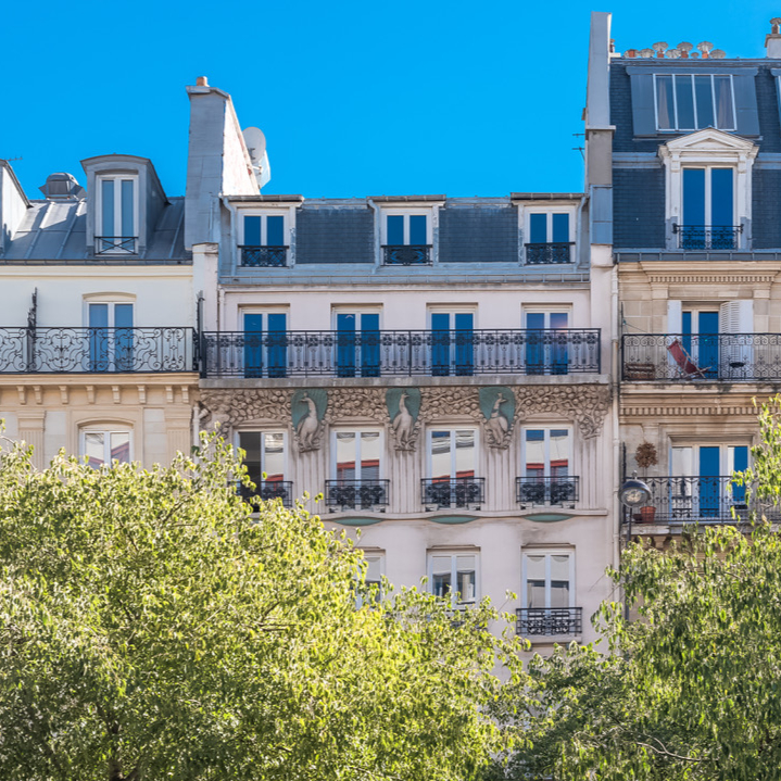 Façades d’immeubles haussmanniens rénovés avec balcons en fer forgé sous un ciel bleu.